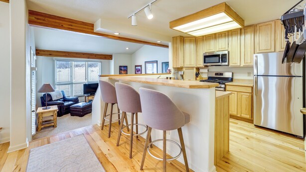 Eine moderne Küche mit Holzschränken, Edelstahlgeräten und einer Bar mit Barhocker.