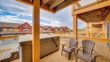 Una terraza de madera con un jacuzzi, dos sillas Adirondack y vistas de casas rojas al fondo.