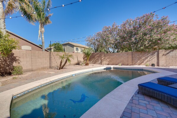 A swimming pool with a dolphin design, surrounded by a brick wall, palm trees, and flowering bushes.
