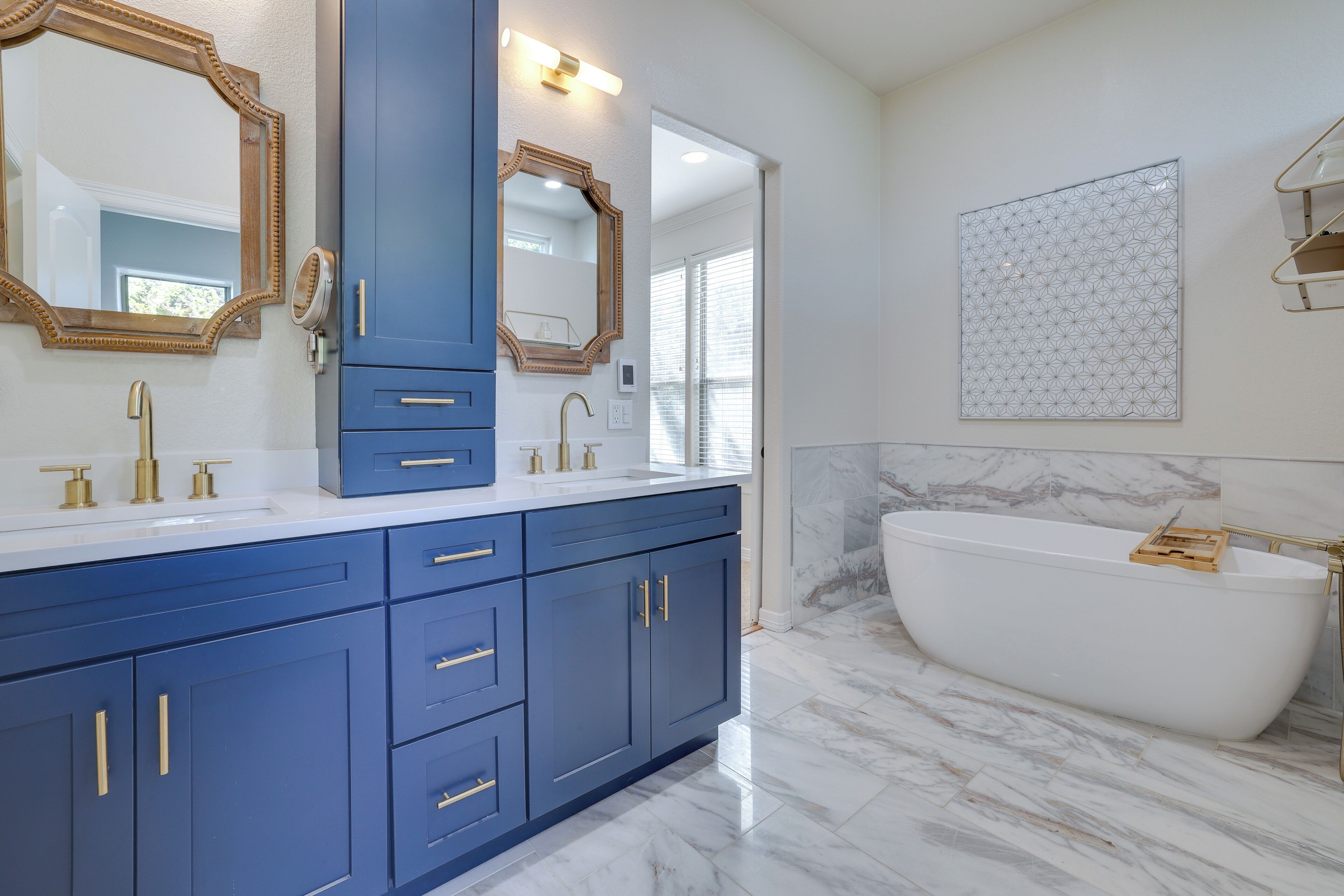 A bathroom with a freestanding bathtub, a double vanity with blue cabinets, and two wall-mounted mirrors.