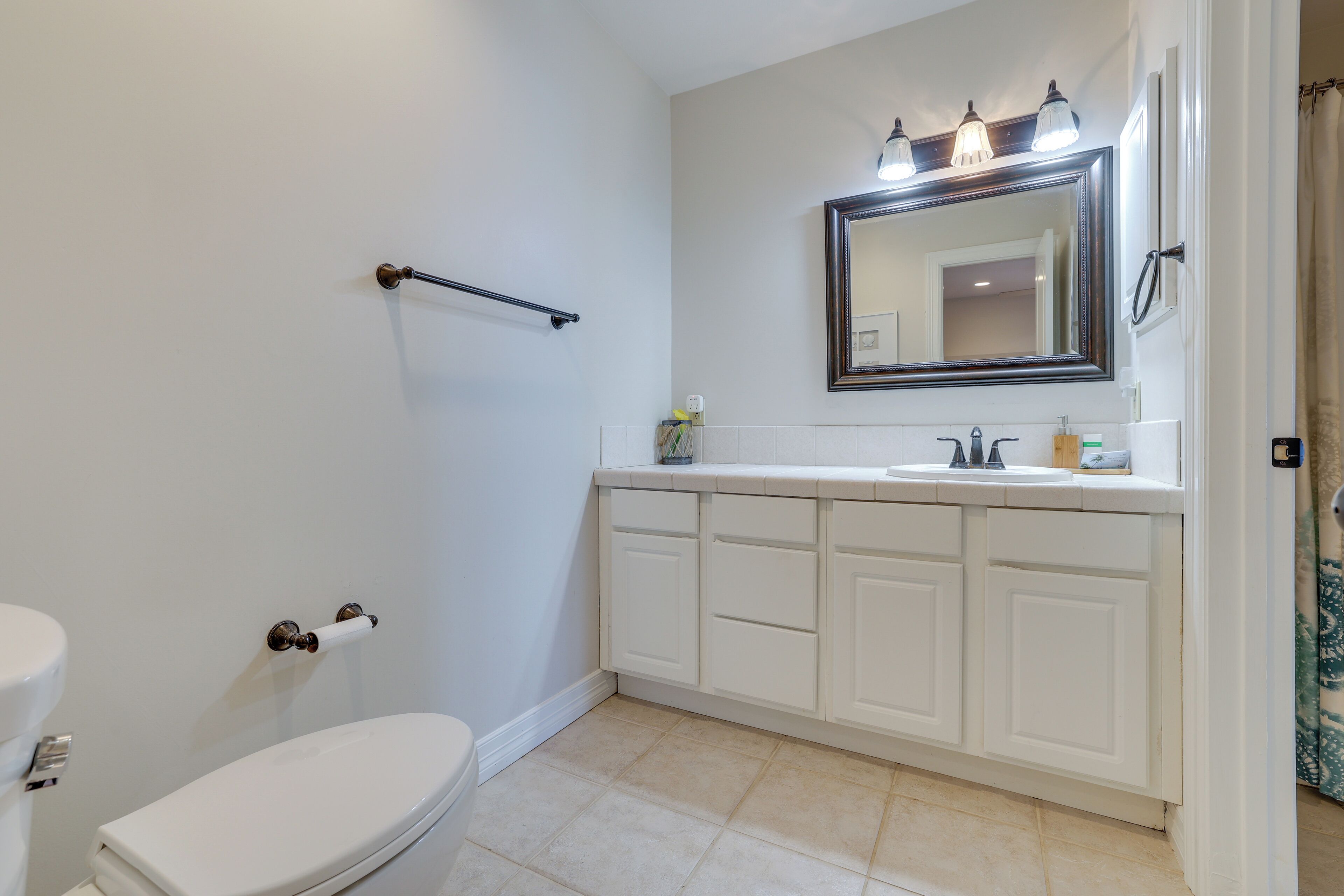 Une salle de bain avec des toilettes blanches, un lavabo surmonté d’un miroir et un porte-serviettes.