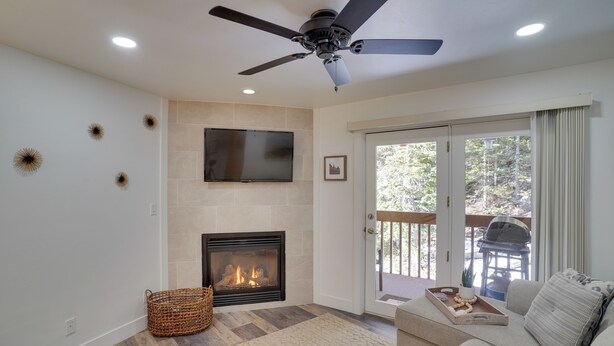A living room with a fireplace, a ceiling fan, a flat-screen TV, and a sliding glass door leading to an outdoor area. - Brian Head Condo w/ Balcony, Grill & Mountain View (Brian Head)
