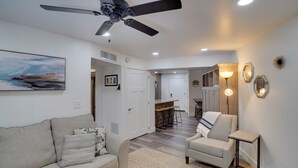 A modern living room with a sofa, armchair, and a ceiling fan. There is a kitchen area in the background with stools and a bar. - Brian Head Condo w/ Balcony, Grill & Mountain View (Brian Head)