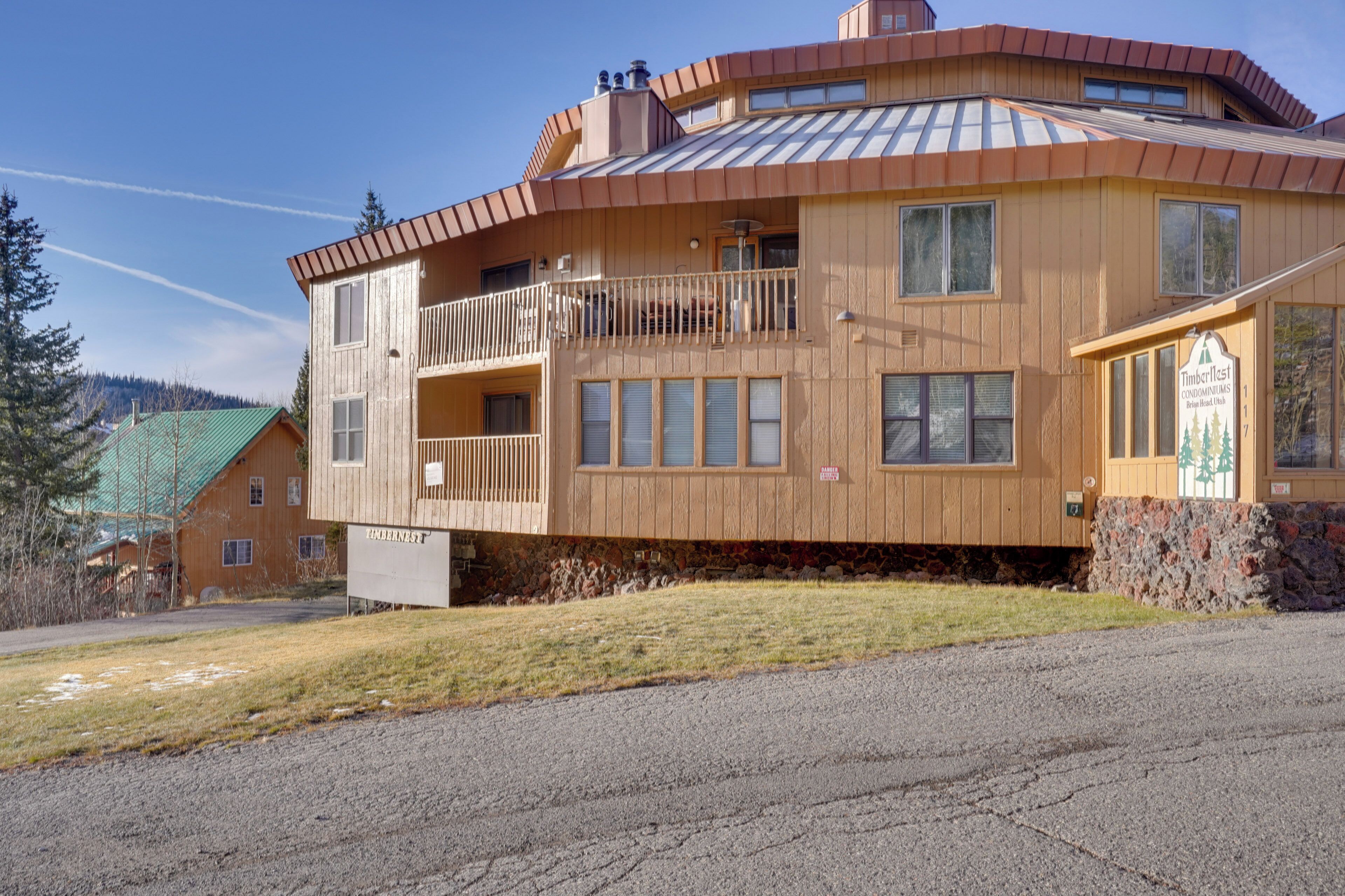 A two-story wooden building with a balcony, a stone foundation, and a sign indicating it is a Timberline condominium.