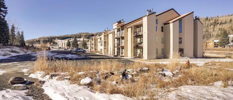 A modern apartment building with multiple balconies, a parking lot, and a snowy landscape.
