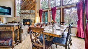 A dining area with a stone fireplace, wooden furniture, and large windows with curtains. - Ski & Golf: Cozy North Conway Mountain Cabin! (North Conway)