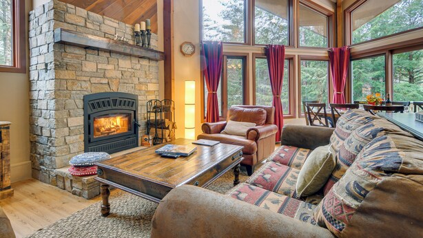 A cozy living room with a stone fireplace, leather sofa, and large windows. - Ski & Golf: Cozy North Conway Mountain Cabin! (North Conway)