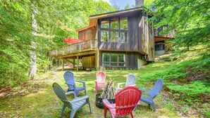A wooden cabin with a deck, surrounded by trees. There are four Adirondack chairs arranged in a circle. - Ski & Golf: Cozy North Conway Mountain Cabin! (North Conway)