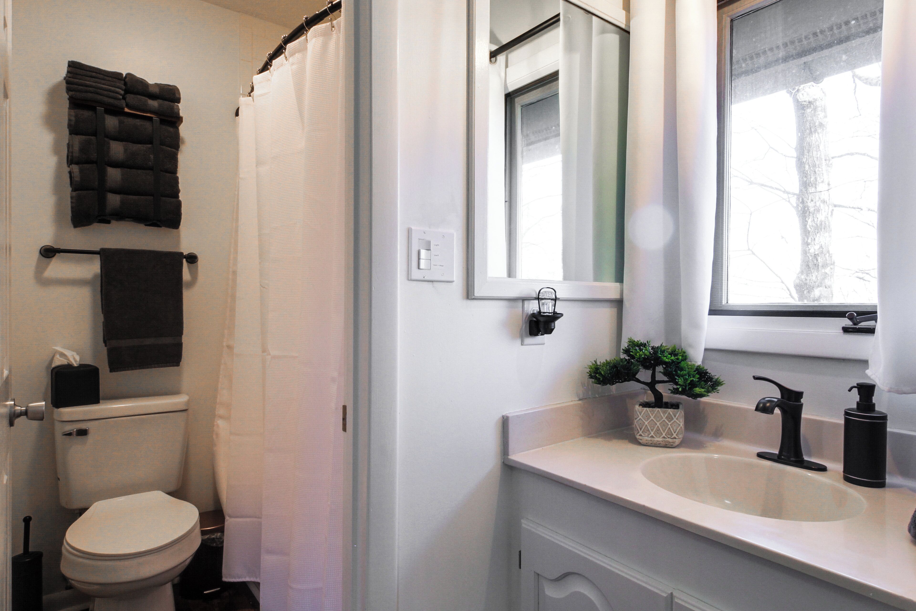 Un baño con inodoro, lavabo, espejo, ventana y cortina de ducha.