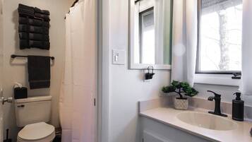A bathroom with a toilet, a sink, a mirror, a window, and a shower curtain.
