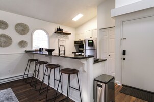 Una cocina moderna con barra, armarios blancos y un refrigerador de acero inoxidable.