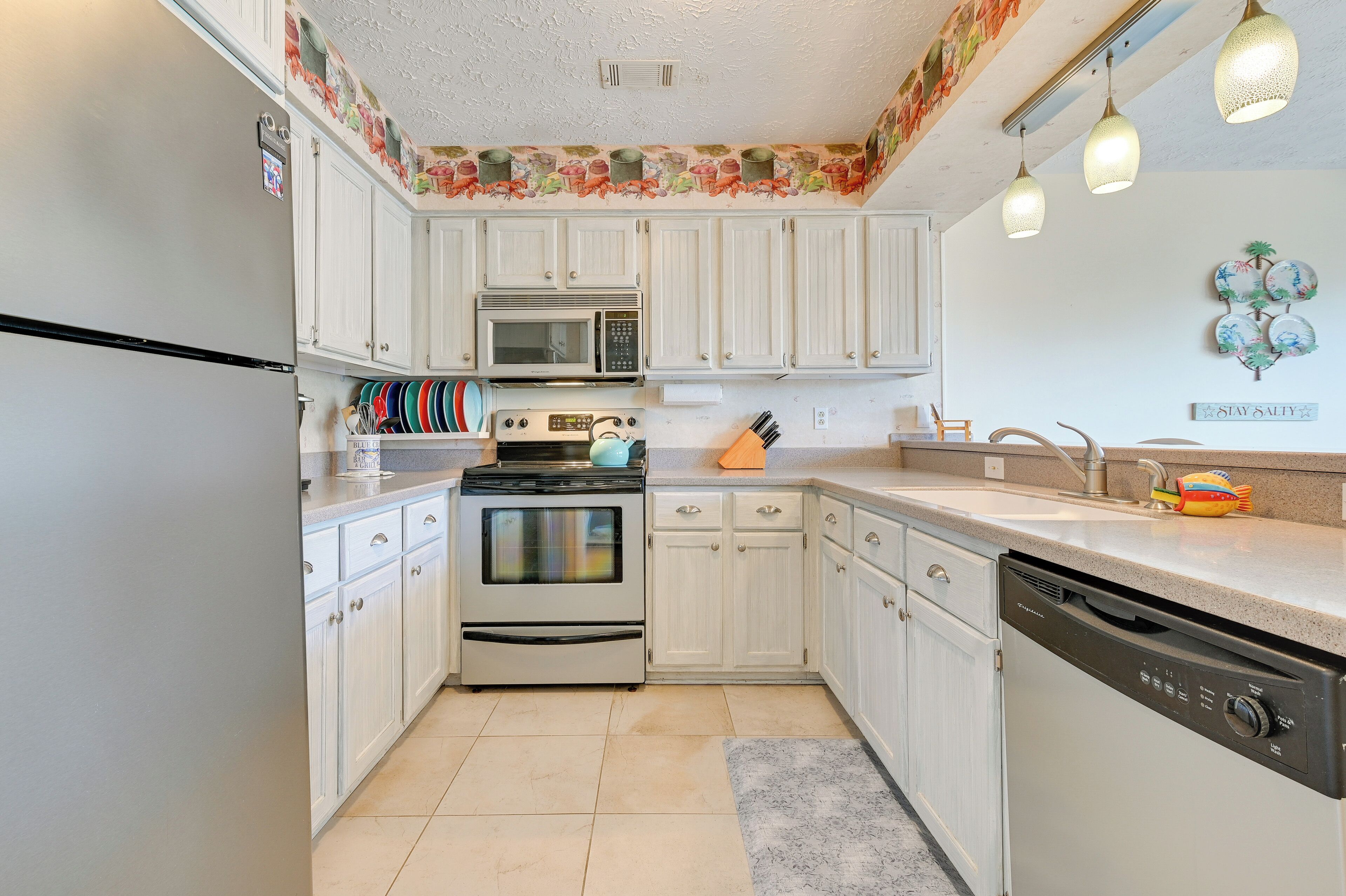 A kitchen with white cabinets, a stainless steel refrigerator, a microwave, an oven, and a dishwasher.