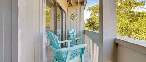 A wooden porch with two turquoise Adirondack chairs and a small table.