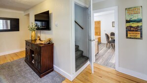 Un couloir avec une armoire en bois, un téléviseur fixé au mur et un escalier menant à une autre pièce.