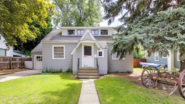 Une maison à deux étages avec un porche à l’avant, un petit jardin devant et une clôture en bois.