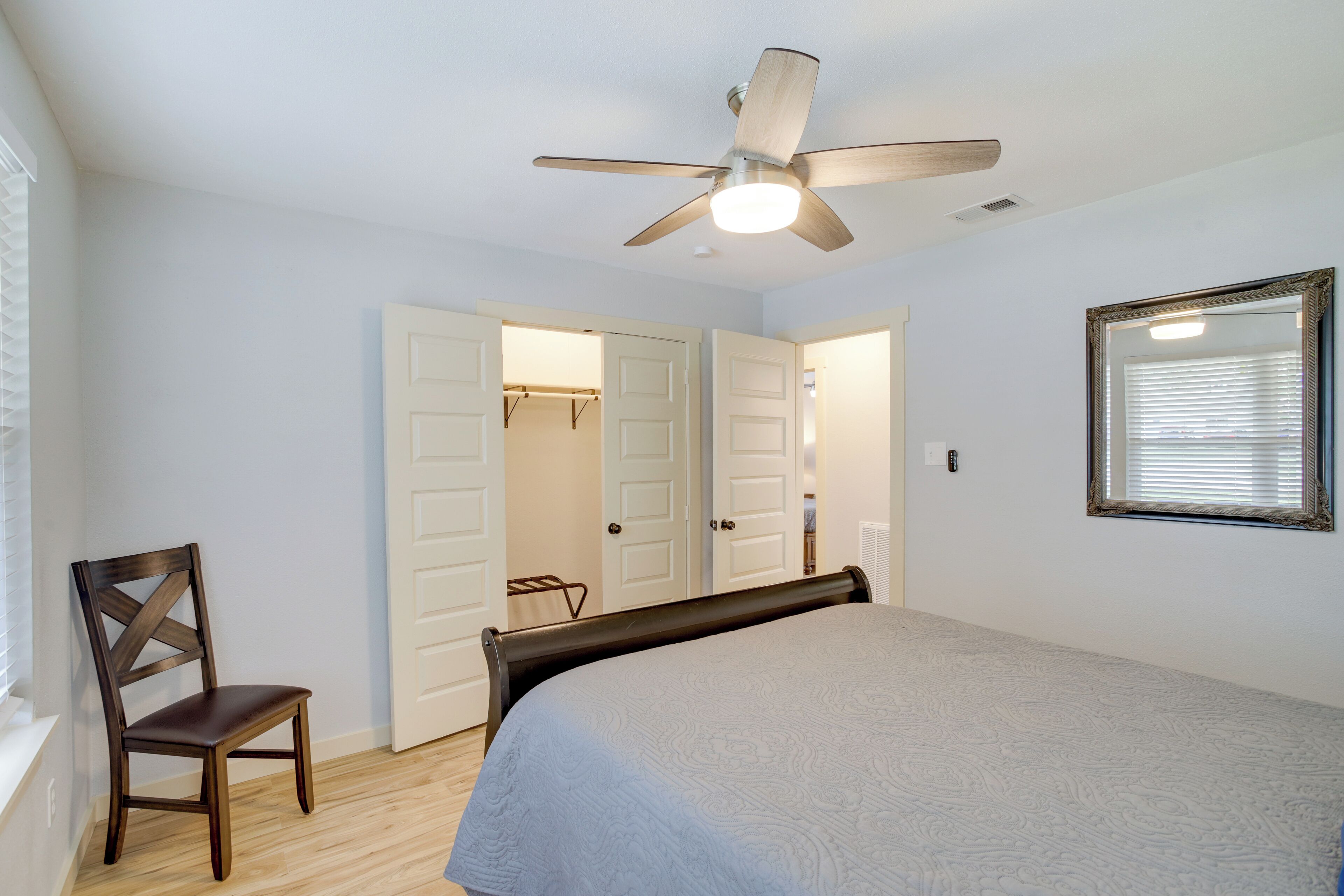 Quarto com cama, uma cadeira, ventilador de teto e janela com persianas.