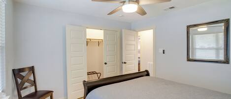 Quarto com cama, uma cadeira, ventilador de teto e janela com persianas.