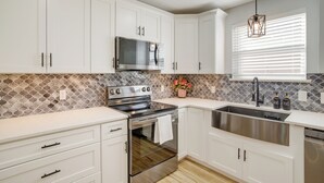 A modern kitchen with white cabinets, a stainless steel stove, and a large window with blinds. - Dog-friendly Home in The Woodlands w/ Fenced Yard! (Conroe)
