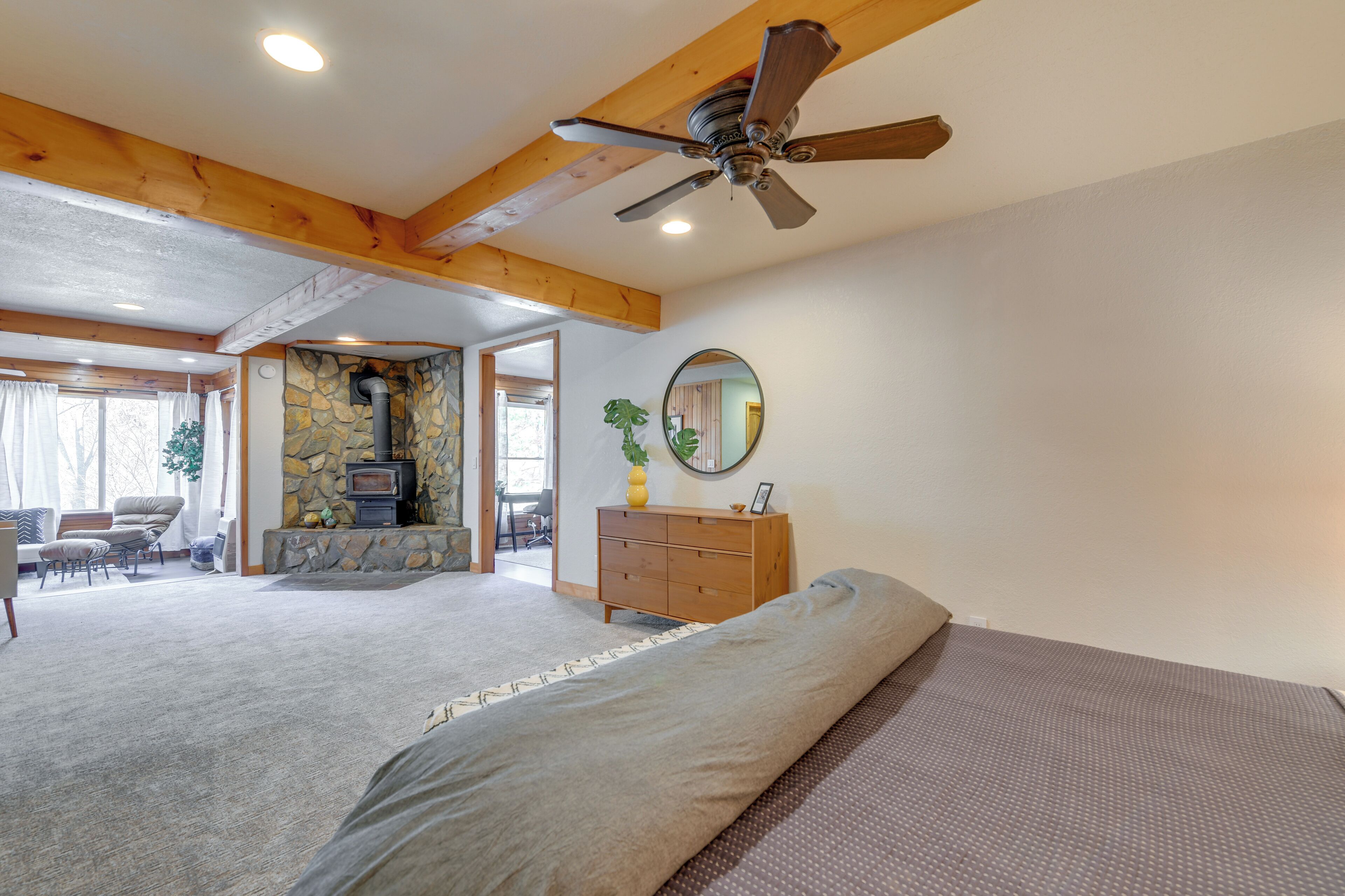 A bedroom with a bed, a dresser, a ceiling fan, and a stone fireplace.