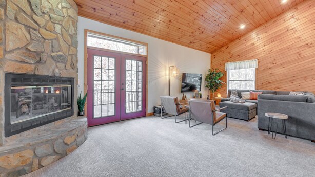 A cozy living room with a stone fireplace, a large window, a grey sofa, and a television. - Mtn-view Waynesville Home Near Trout Stocked Creek (Waynesville)