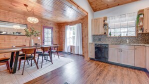 A wooden interior with a dining area, kitchen, and a large window with curtains. - Mtn-view Waynesville Home Near Trout Stocked Creek (Waynesville)