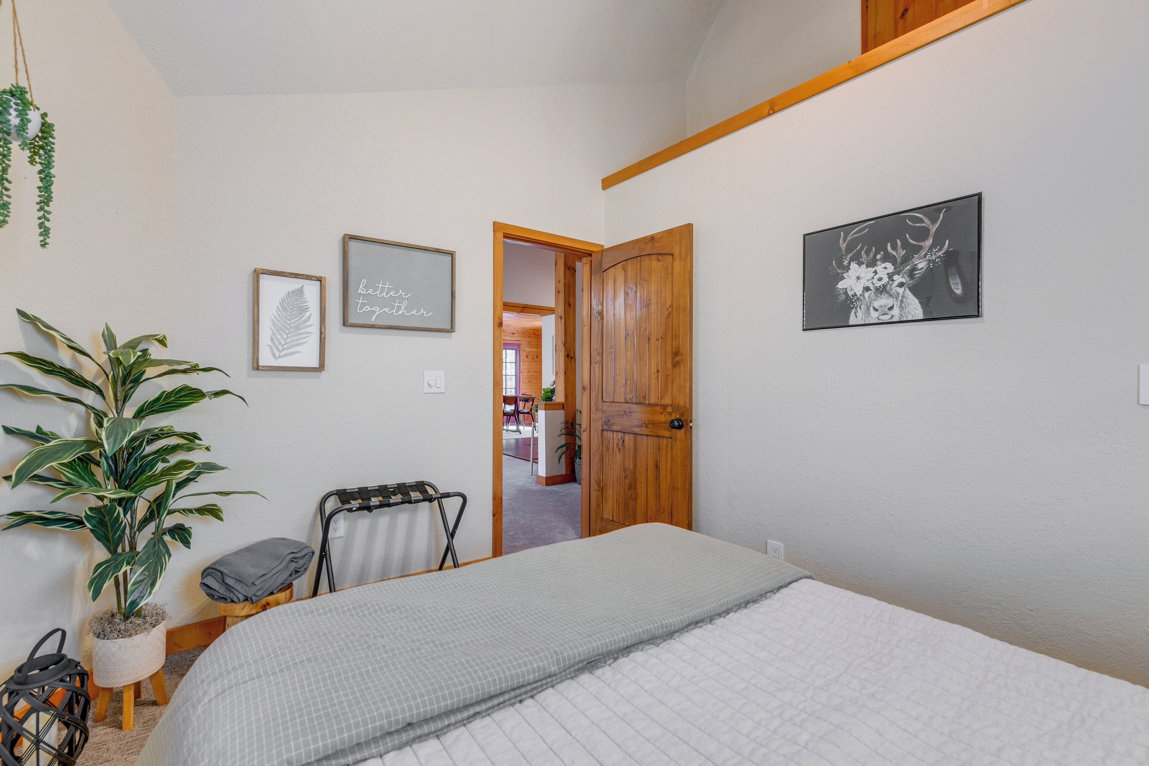 Une chambre à coucher avec un lit, une porte en bois, une plante en pot et des tableaux encadrés accrochés au mur.