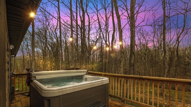 Ein Whirlpool auf einer Holzterrasse mit Blick auf Bäume und einen Sonnenuntergang.