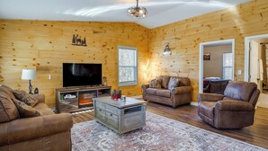 Ein gemütliches Wohnzimmer mit Holzwänden, einem Flachbildfernseher, Ledersofas und einem gemusterten Teppich.