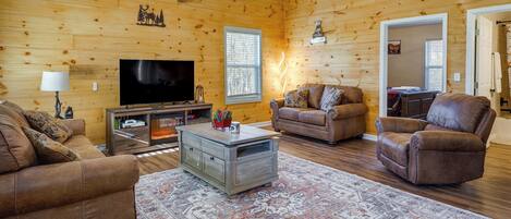 A cozy living room with wooden walls, a flat-screen TV, leather sofas, and a patterned rug.
