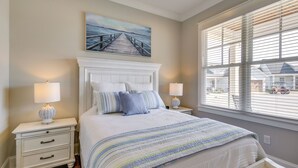 A bedroom with a large bed, two bedside tables, a painting of a pier, and a window with blinds. - Lake Access & Boat Slip: Greenwood Cottage! (Greenwood)