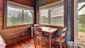 Uma cabana de madeira com uma mesa de jantar e cadeiras, janelas amplas e vista para o exterior.