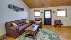 A living room with a brown leather sofa, a wooden coffee table, and a patterned rug. There are two armchairs and a door with windows. - Pet-friendly Cabin w/ Fire Pit in Spruce Pine! (Spruce Pine)
