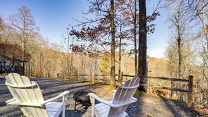 Two Adirondack chairs facing a fire pit in a wooded area with a wooden fence. - Pet-friendly Cabin w/ Fire Pit in Spruce Pine! (Spruce Pine)