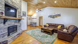 A living room with a stone fireplace, wooden ceiling, and a brown leather sofa. - Pet-friendly Cabin w/ Fire Pit in Spruce Pine! (Spruce Pine)