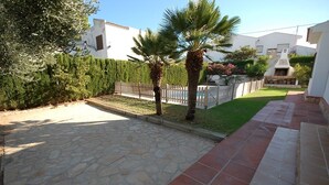 Un camino pavimentado que conduce a un edificio blanco con un patio de piedra y un pequeño césped.