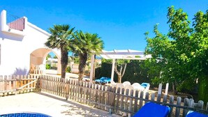 Una piscina con sillones de descanso, una valla de madera y una pérgola.