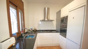 Una cocina compacta con horno integrado, extractor de acero inoxidable y refrigerador blanco.