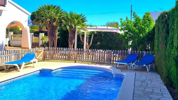 Una piscina con azulejos azules, rodeada por una valla de madera y dos sillas reclinables azules.