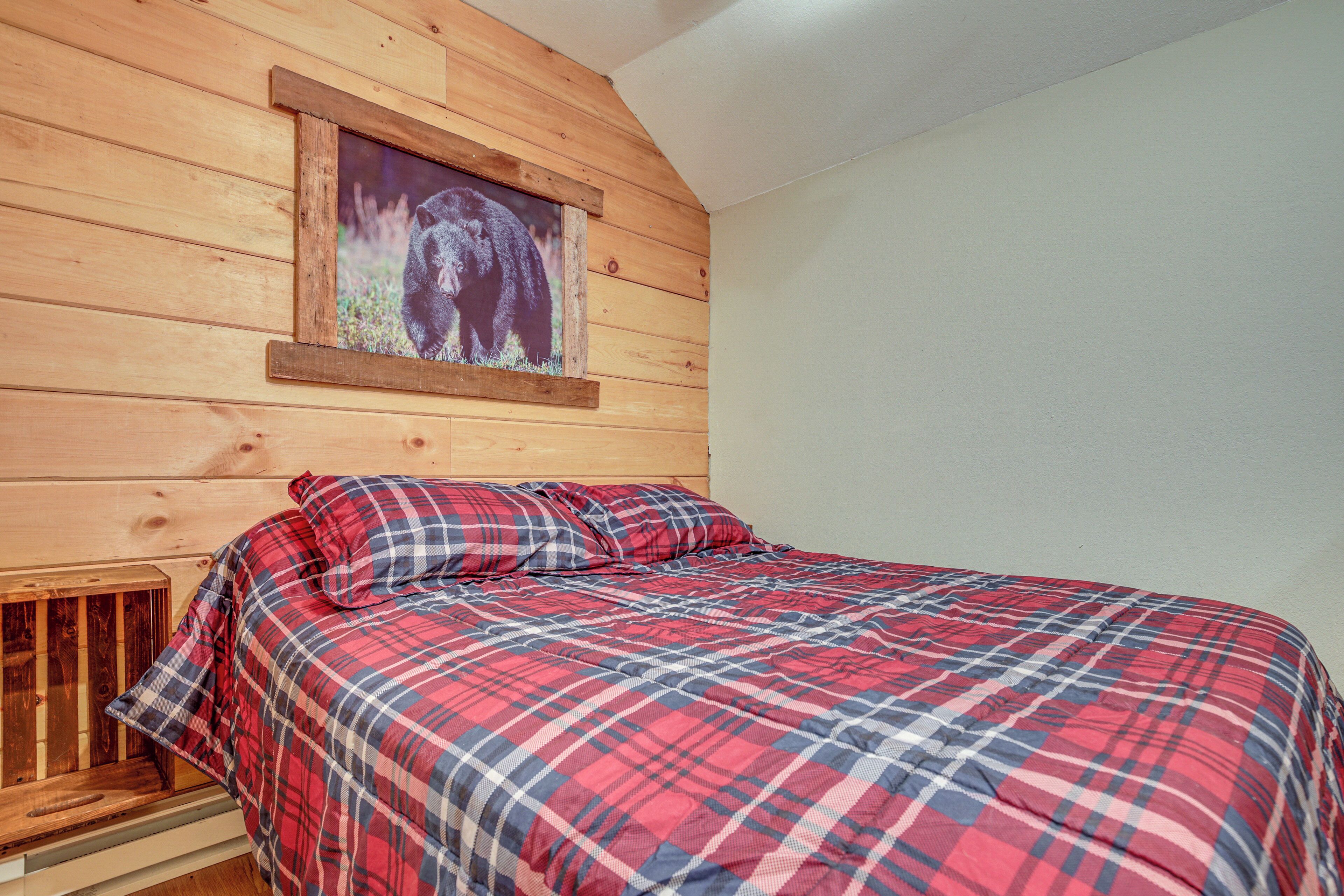 Une chambre à coucher avec une tête de lit en bois, une couvre-lit à carreaux et un tableau représentant un ours accroché au mur.