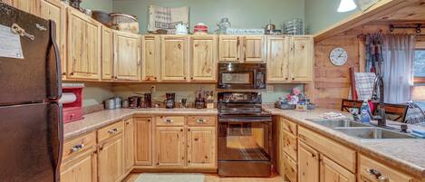 A kitchen with wooden cabinets, a refrigerator, a microwave, an oven, and a sink.