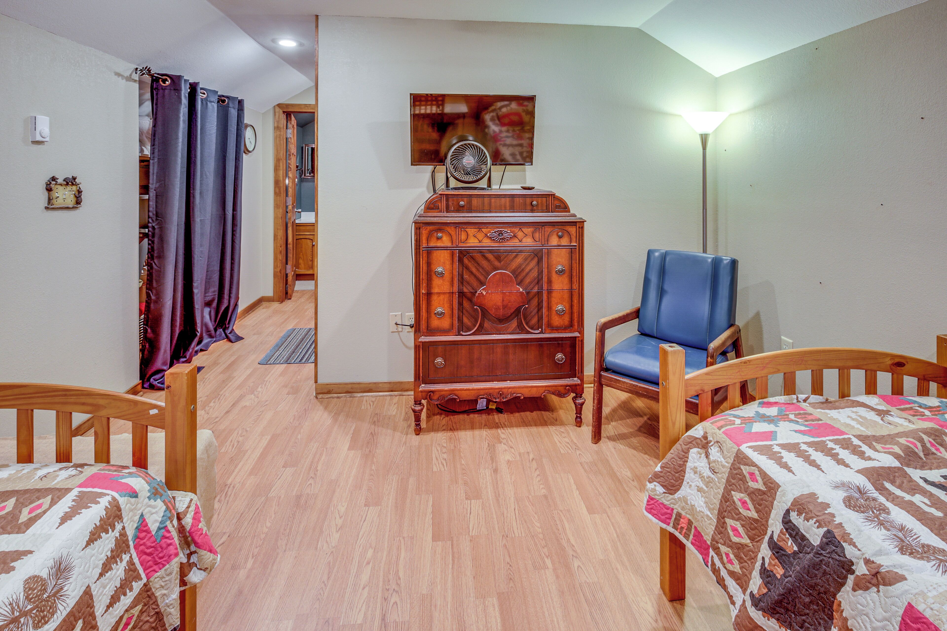 Una habitación con dos camas de madera, un aparador de madera, una silla azul y una lámpara.