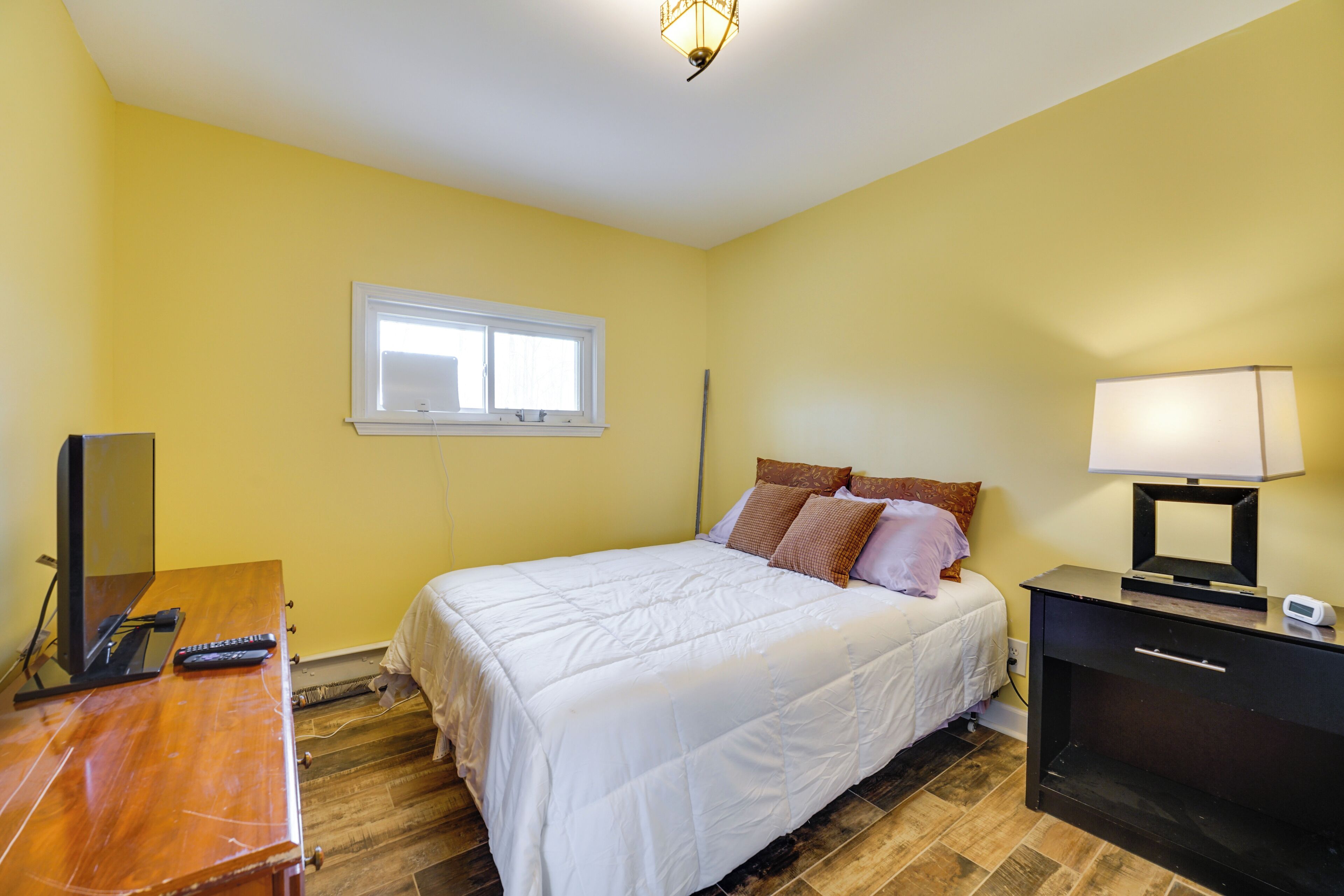 Une chambre à coucher avec un lit, une table de chevet, une lampe et une fenêtre.