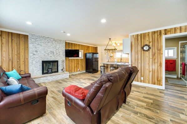 A modern living room with a fireplace, leather sofas, and a kitchen area visible through an open doorway. - Quiet Country Home By Shay Lake! (Silverwood)