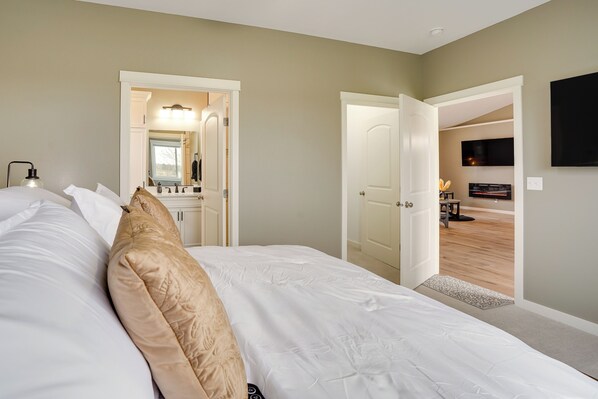 Une chambre avec un grand lit, une salle de bain avec un miroir et un lavabo, et un téléviseur dans la pièce adjacente.