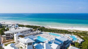 Resort com ampla área de piscina, vários edifícios com telhados brancos e uma praia com espreguiçadeiras.