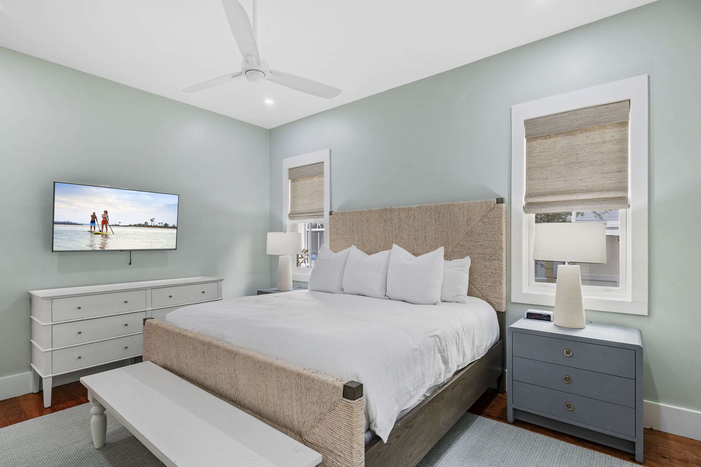 A bedroom with a bed, a bedside table, a nightstand, a TV, and a ceiling fan.