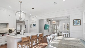 Cozinha moderna com ilha central, armários brancos e área de refeições com mesa de mármore.