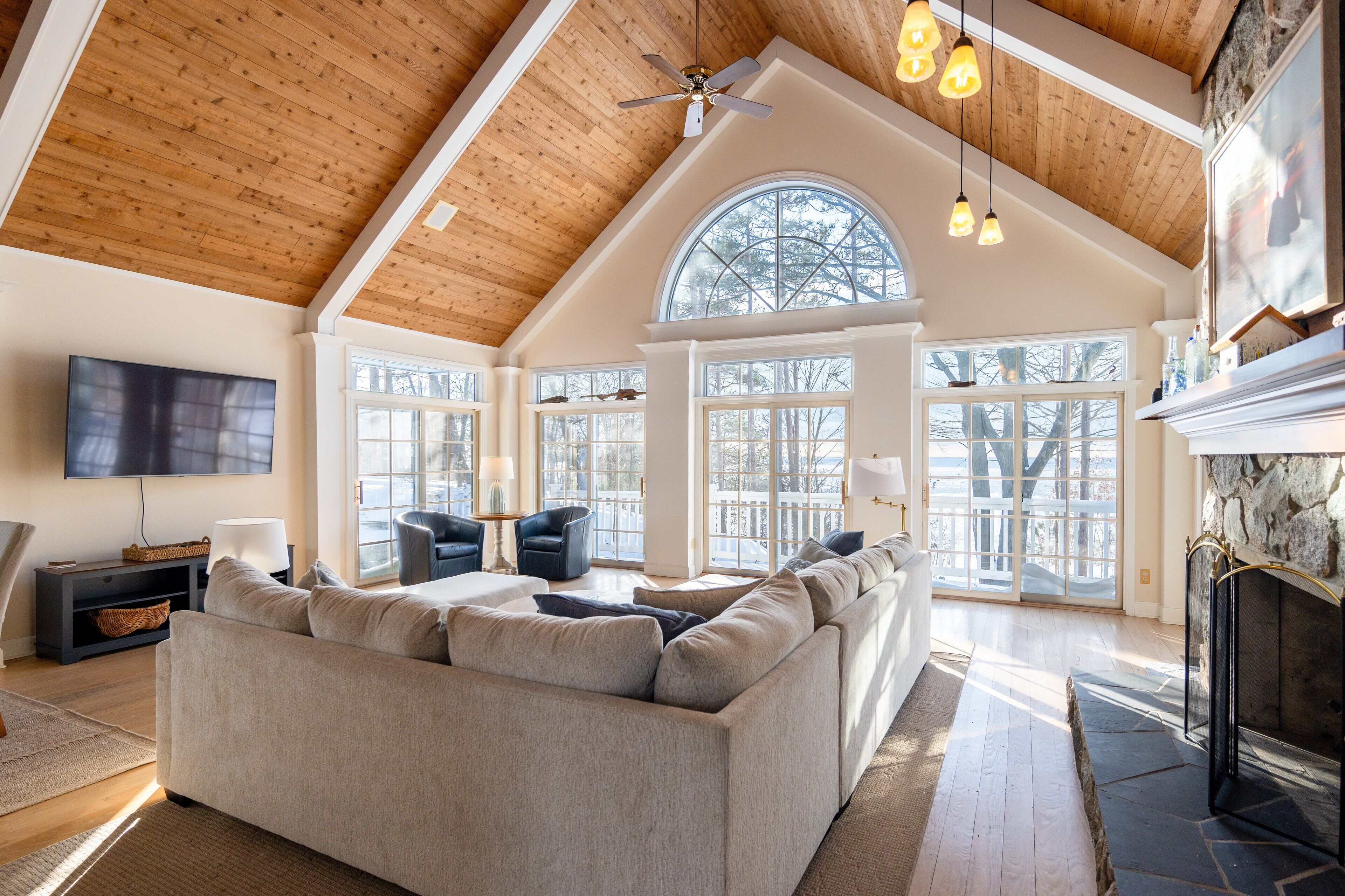 A spacious living room with a high ceiling, large windows, a fireplace, and a modern sofa.