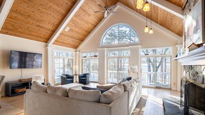 A spacious living room with a high ceiling, large windows, a fireplace, and a modern sofa. - Beautiful Lake Michigan Home Great for Large (West Olive)