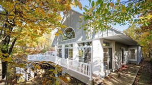 A white wooden house with large windows and a porch, surrounded by autumn foliage. - Beautiful Lake Michigan Home Great for Large (West Olive)